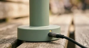 Close-up of a battery powered hand fan charging via a USB-C cable on a wooden surface with a glowing indicator light.