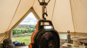 A close-up of a rechargeable fan for camping hanging securely from a central tent pole using a built-in carabiner hook.