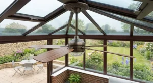 Five-blade dark timber conservatory ceiling fan installed in a classic brick dwarf-wall Edwardian conservatory with views of a British garden.
