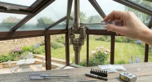 A brass conservatory ceiling fan with a long downrod suspended from the central ridge of a high-pitched Victorian glass conservatory roof.
