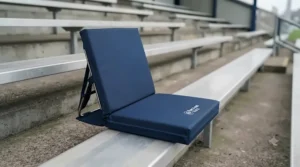 Padded bleacher cushion with a sturdy adjustable backrest providing lumbar support on a cold metal stadium terrace.
