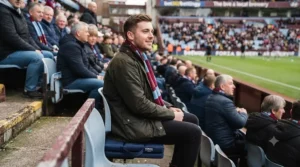 Football supporter sitting comfortably on a padded stadium seat cushion in the stands.