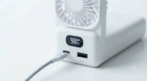 A lightweight, foldable power bank fan shown next to a handbag and passport to demonstrate its travel-friendly size.