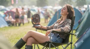 Camper using a lightweight personal USB fan while relaxing in a camp chair at a UK outdoor festival.