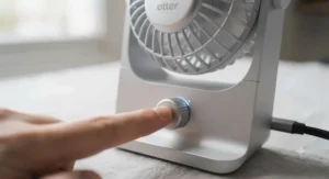 A finger pressing the multi-speed control button on the base of a modern USB-C desk fan